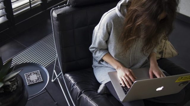 膝の上にノートパソコンを置いてソファーで作業をする女性